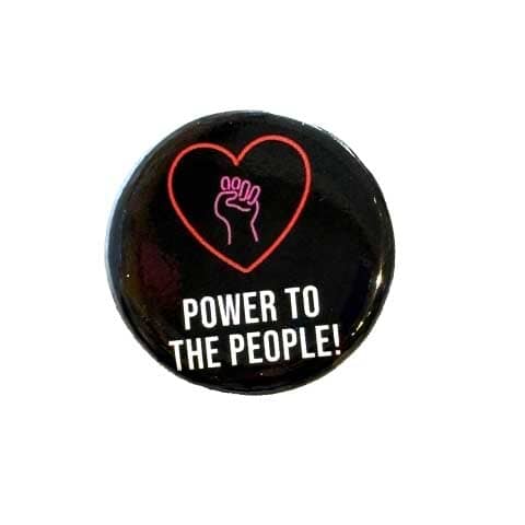 Button badge with heart and solidarity fist design and 'Power to the People!' text on a black background