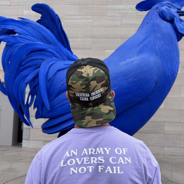 Person wearing a cap and t-shirt with text, standing next to a large blue sculpture.