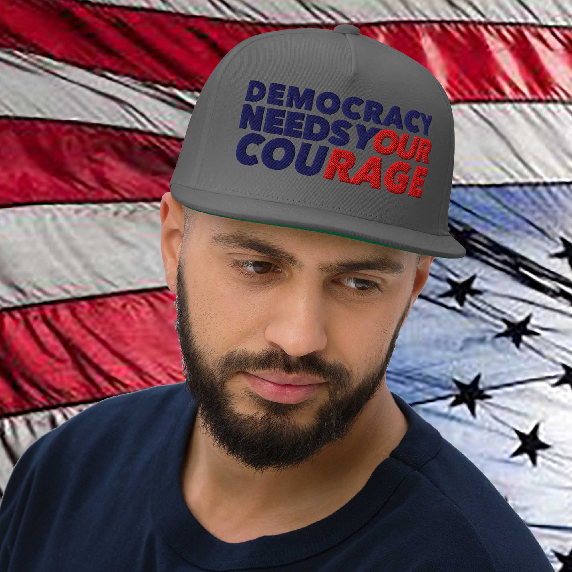 Man wearing a cap with 'Democracy Needs Your Courage' text in front of an American flag.