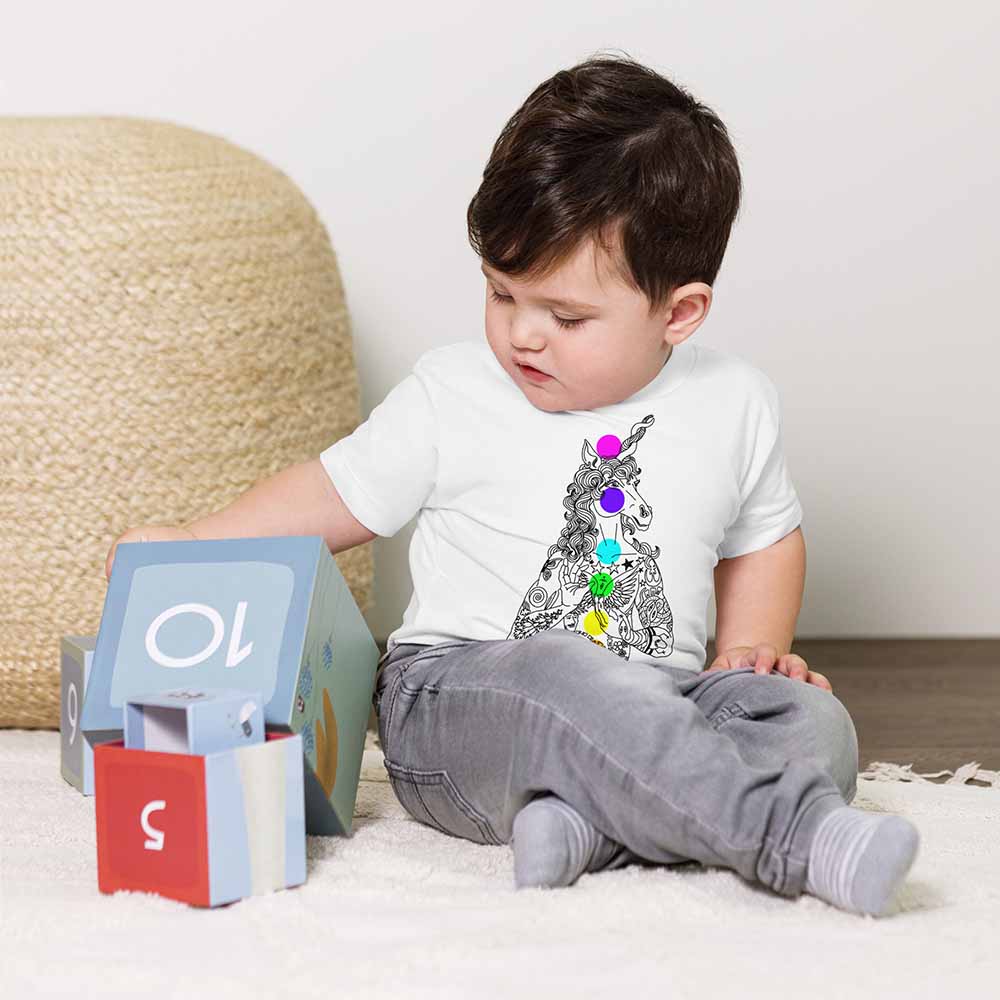 Child sitting on a carpeted floor with a colorful unicorn design on a white shirt.