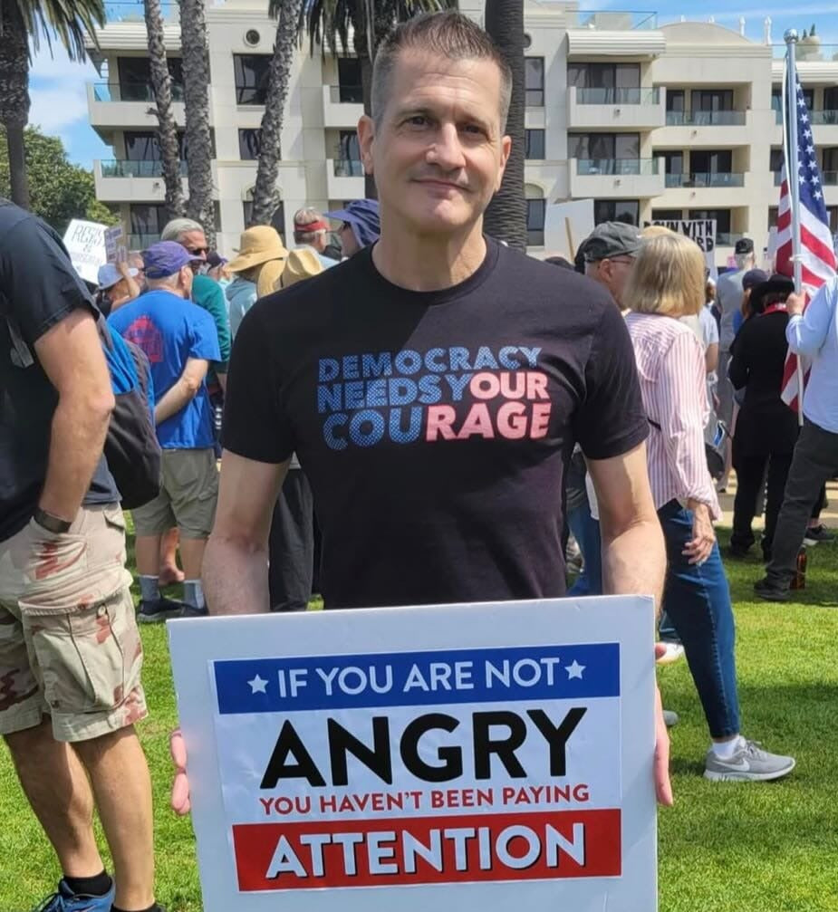 A customer at a protest wearing the black Democracy Needs Your Courage tee