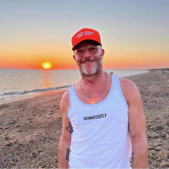 adam singer wearing a blaze orange cap reading shoot loads not guns and white tank top with &