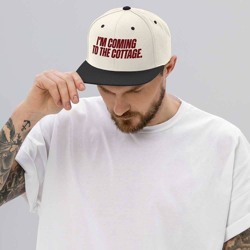 Man wearing a cap with 'I'm Coming to the Cottage' text on a plain background