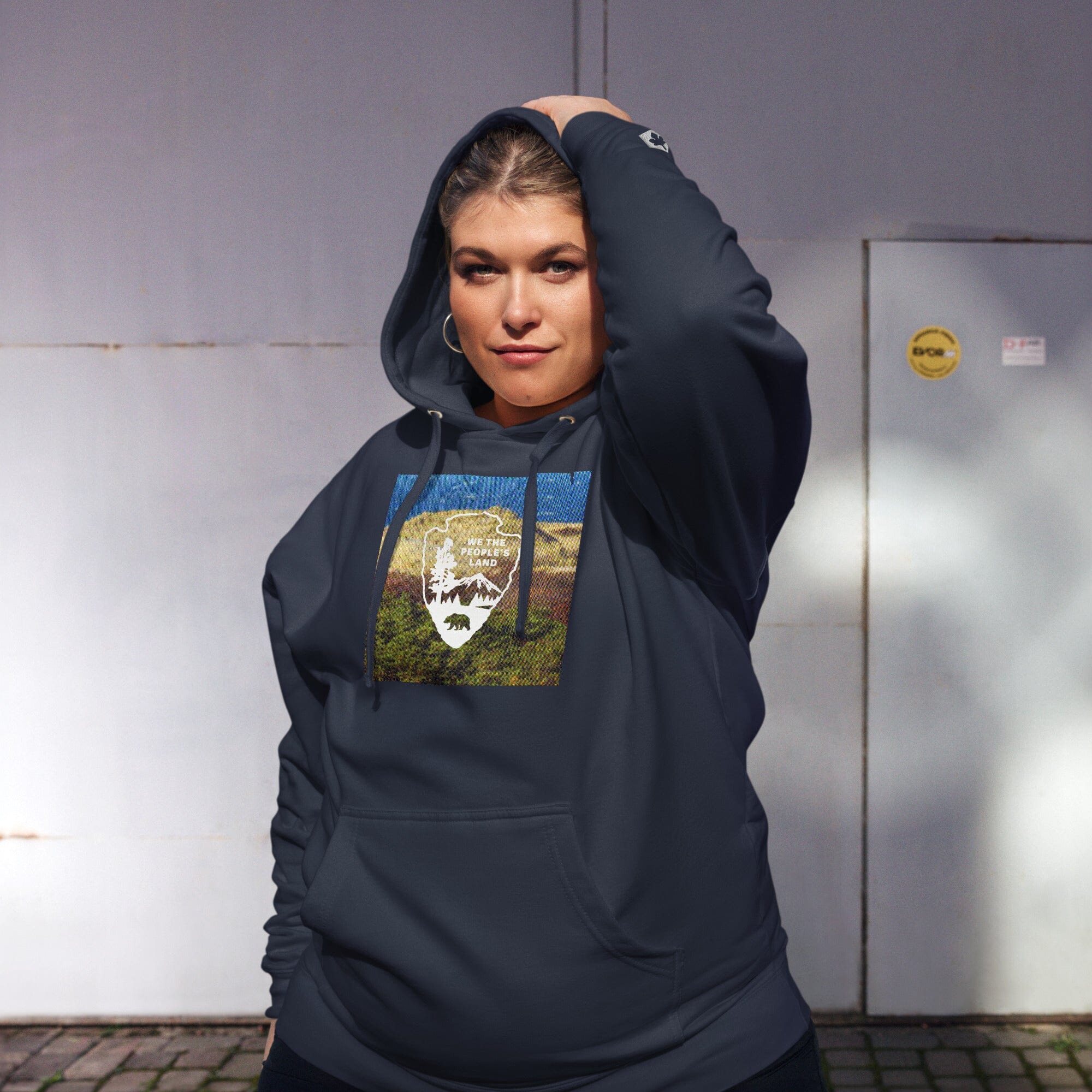 Person wearing a dark hoodie with a graphic design, standing against a plain wall.